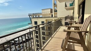A balcony with a view of the ocean, wooden chairs, and a building with multiple floors and balconies. - All Bedrooms w/ Balcony & Golf Views on the 15th Floor, Free Golf Daily (Panama City Beach)