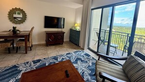 Sala de estar con televisor, mesa de comedor, sillas, sofá y balcón con vistas.