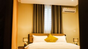 A hotel room with a bed, two bedside tables with lamps, a window with curtains, and an air conditioning unit. - Fully furnished and spacious 2bedroom House in Accra (Nii Okaiman East)