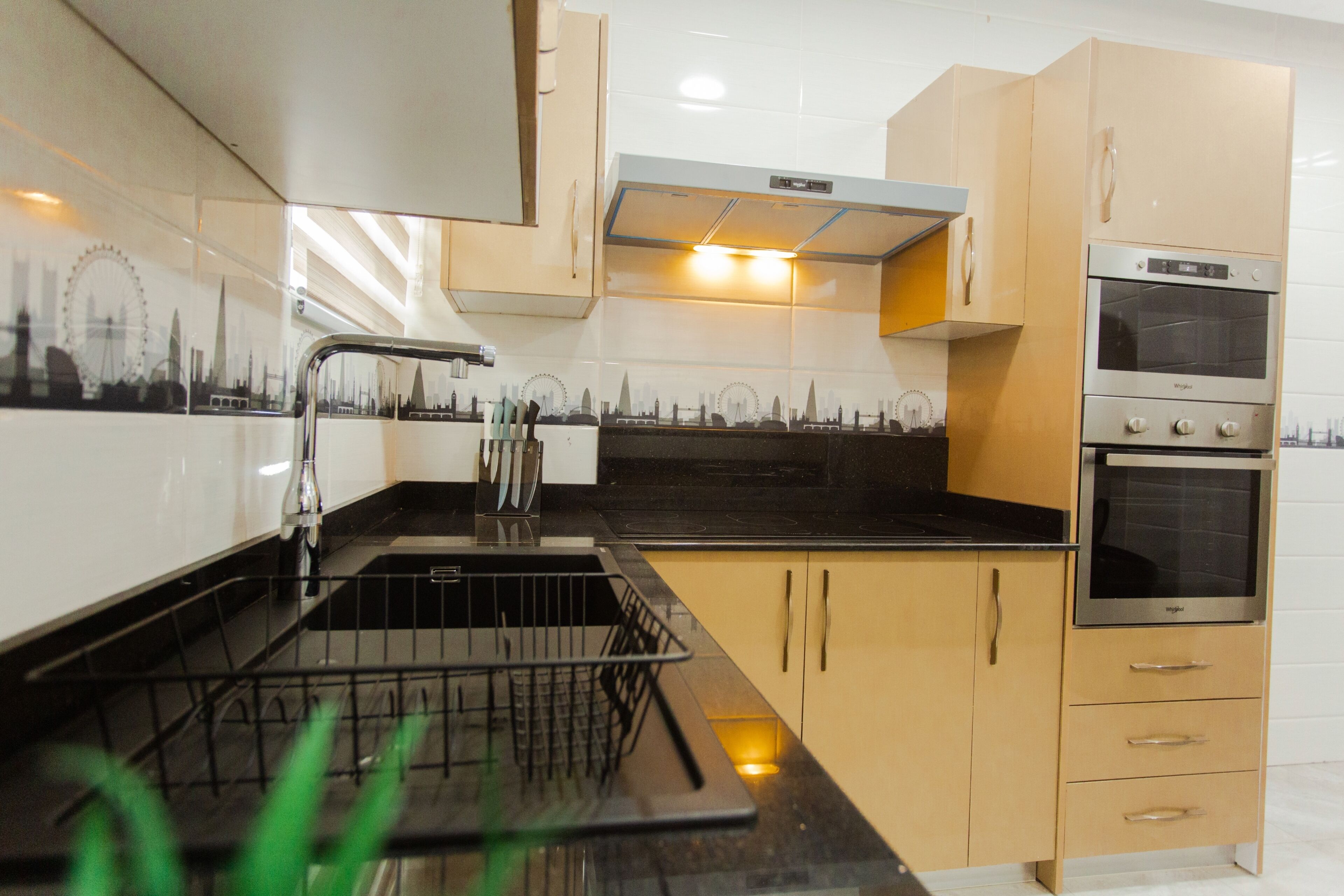 A modern kitchen with a black countertop, stainless steel appliances, and a cityscape backsplash.
