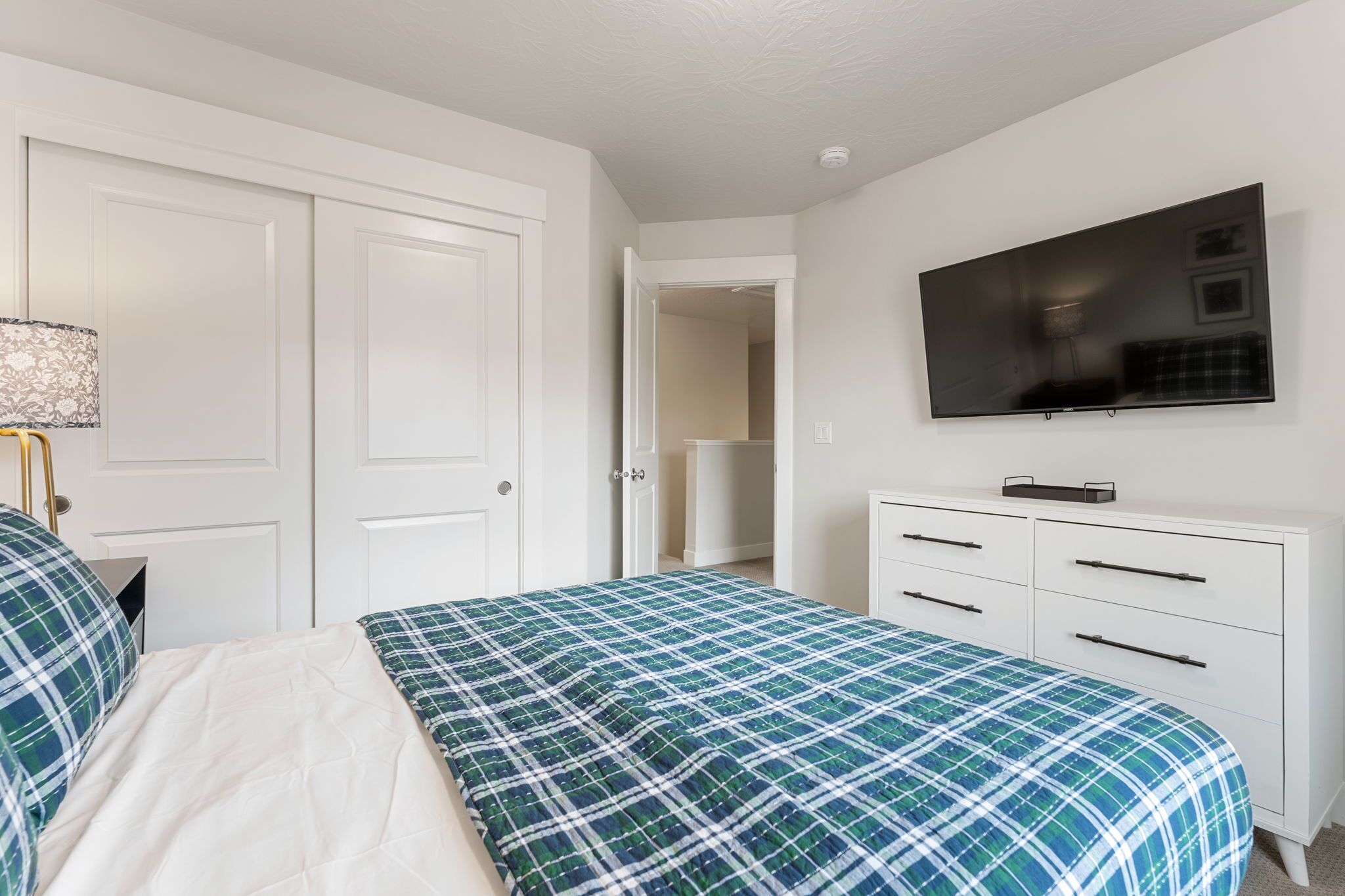 A bedroom with a bed, a dresser, a television, and a door.