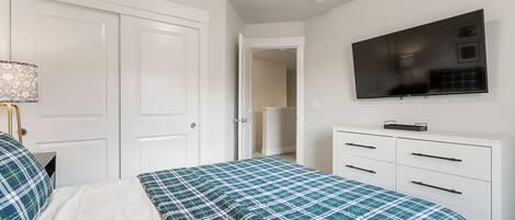 A bedroom with a bed, a dresser, a television, and a door.