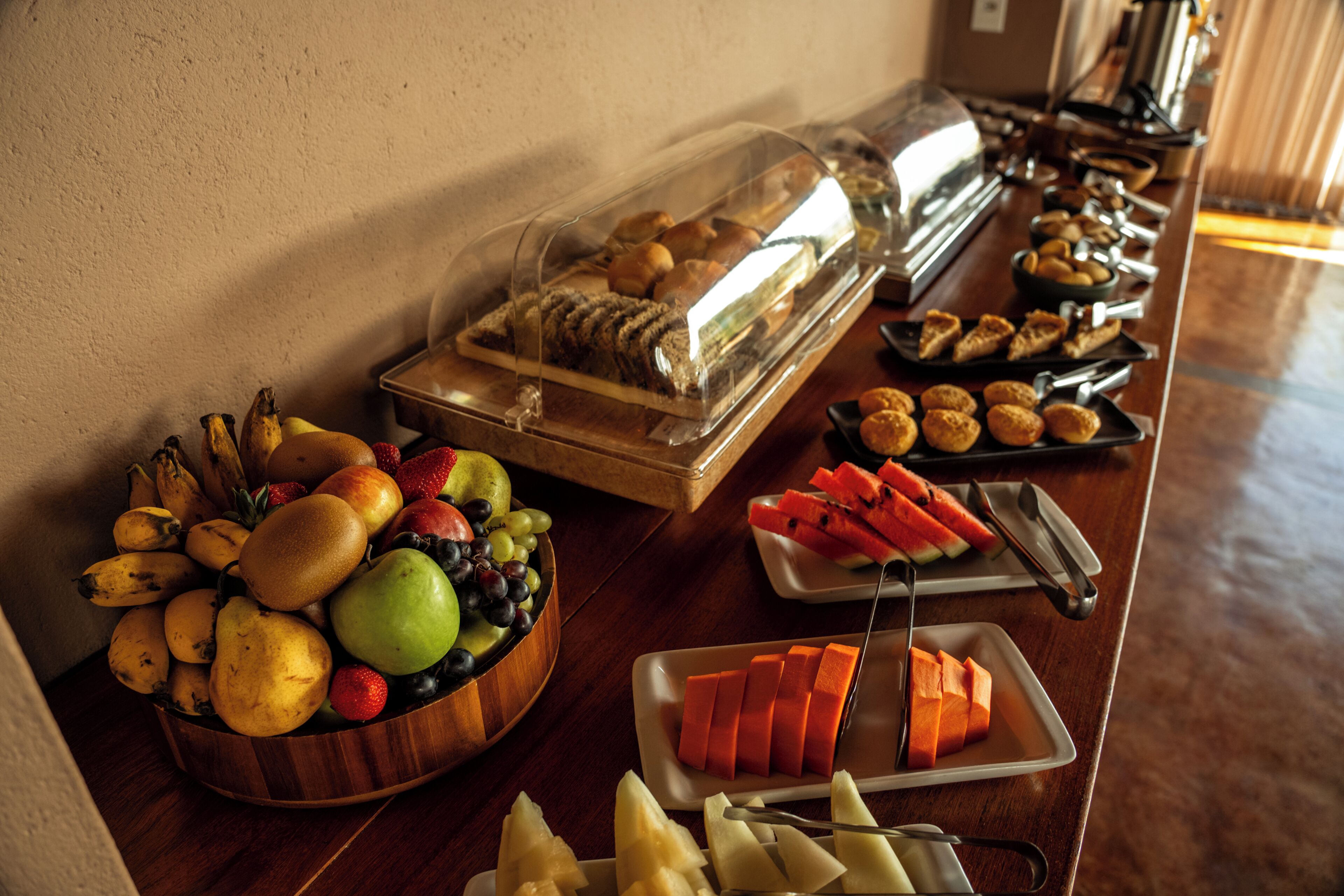 Buffet com diversas frutas, doces e pães.