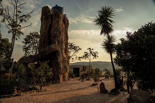 Paisaje desértico con una gran formación rocosa, cactus y un edificio de diseño moderno.