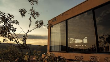Un edificio con grandes ventanales, terraza al aire libre y vegetación circundante.