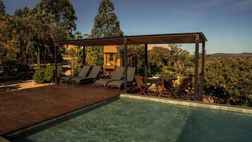 A pool area with a wooden deck, lounge chairs, and a covered seating area.
