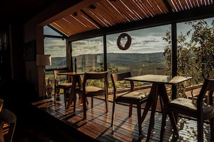 Uma sala de jantar com vista para o campo, com uma mesa, cadeiras, uma coroa pendurada e teto de madeira.