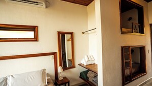 Habitación de hotel con cama, mesita de noche con lámpara, espejo, repisa con toallas y ventana con vista al exterior.