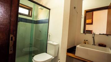 Uma casa de banho com cabine de duche em vidro, sanita e lavatório com espelho em cima.