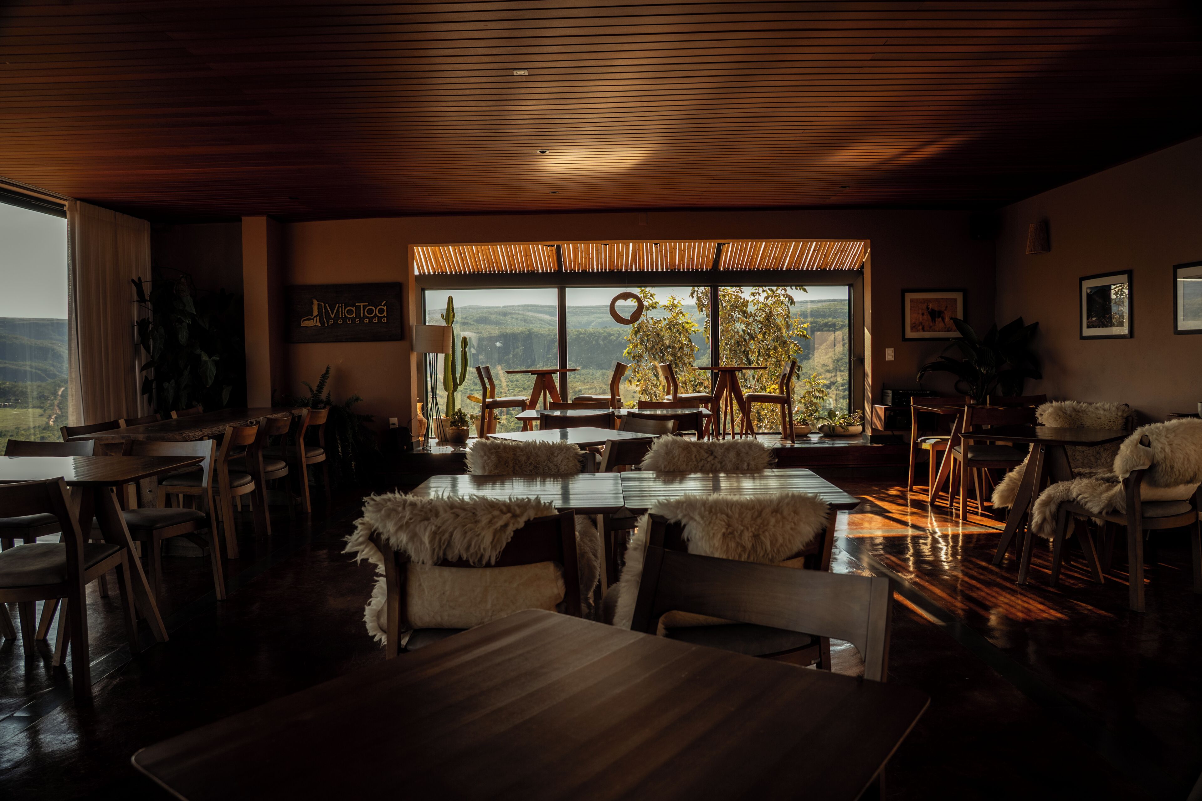 A dining area with wooden tables and chairs, a large window with a view of the landscape, and a sign on the wall.