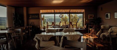 A dining area with wooden tables and chairs, a large window with a view of the landscape, and a sign on the wall.