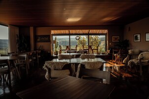 A dining area with wooden tables and chairs, a large window with a view of the landscape, and a sign on the wall.