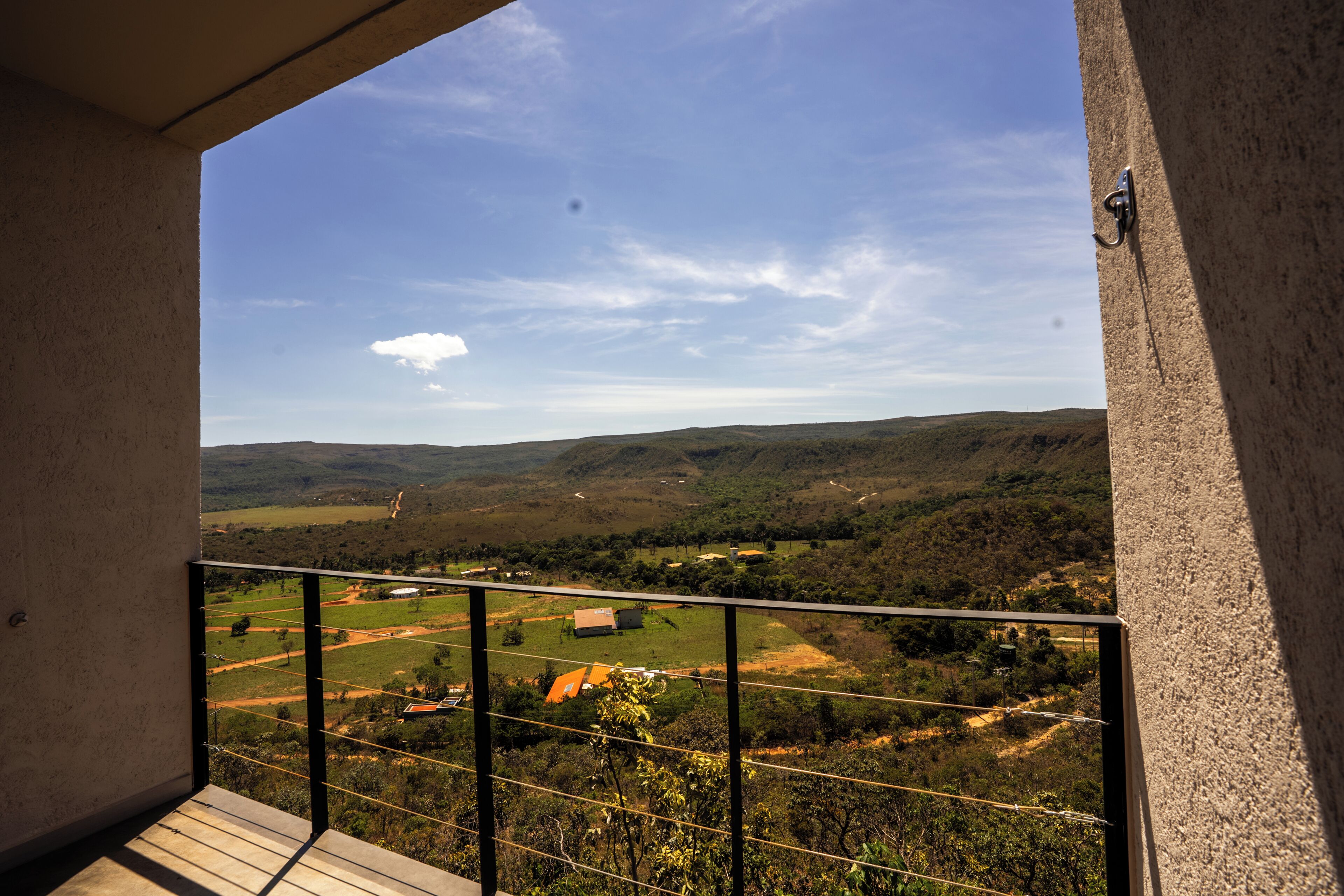 A balcony with a view of a hilly landscape, a clear sky, and a distant road.