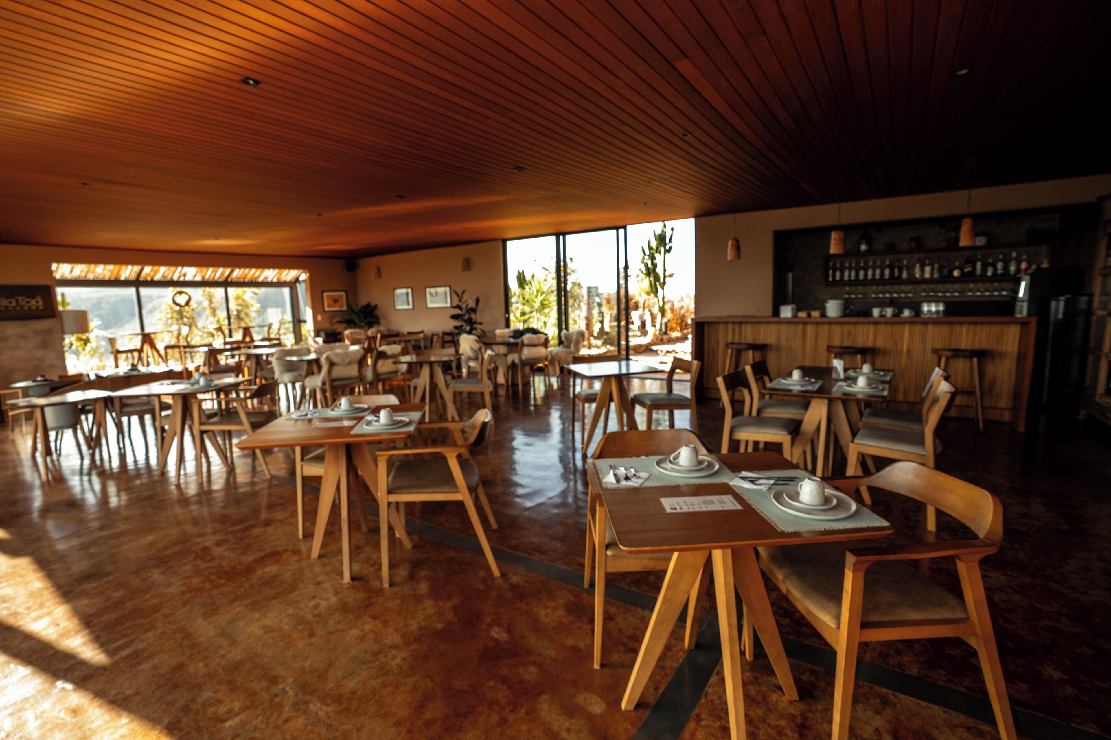 Een ruim restaurant met houten tafels en stoelen, een bar en grote ramen voor natuurlijk licht.
