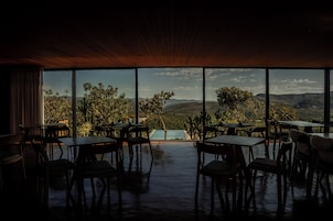 Uma área de refeições com mesas e cadeiras voltada para uma grande janela com vista para uma paisagem montanhosa.
