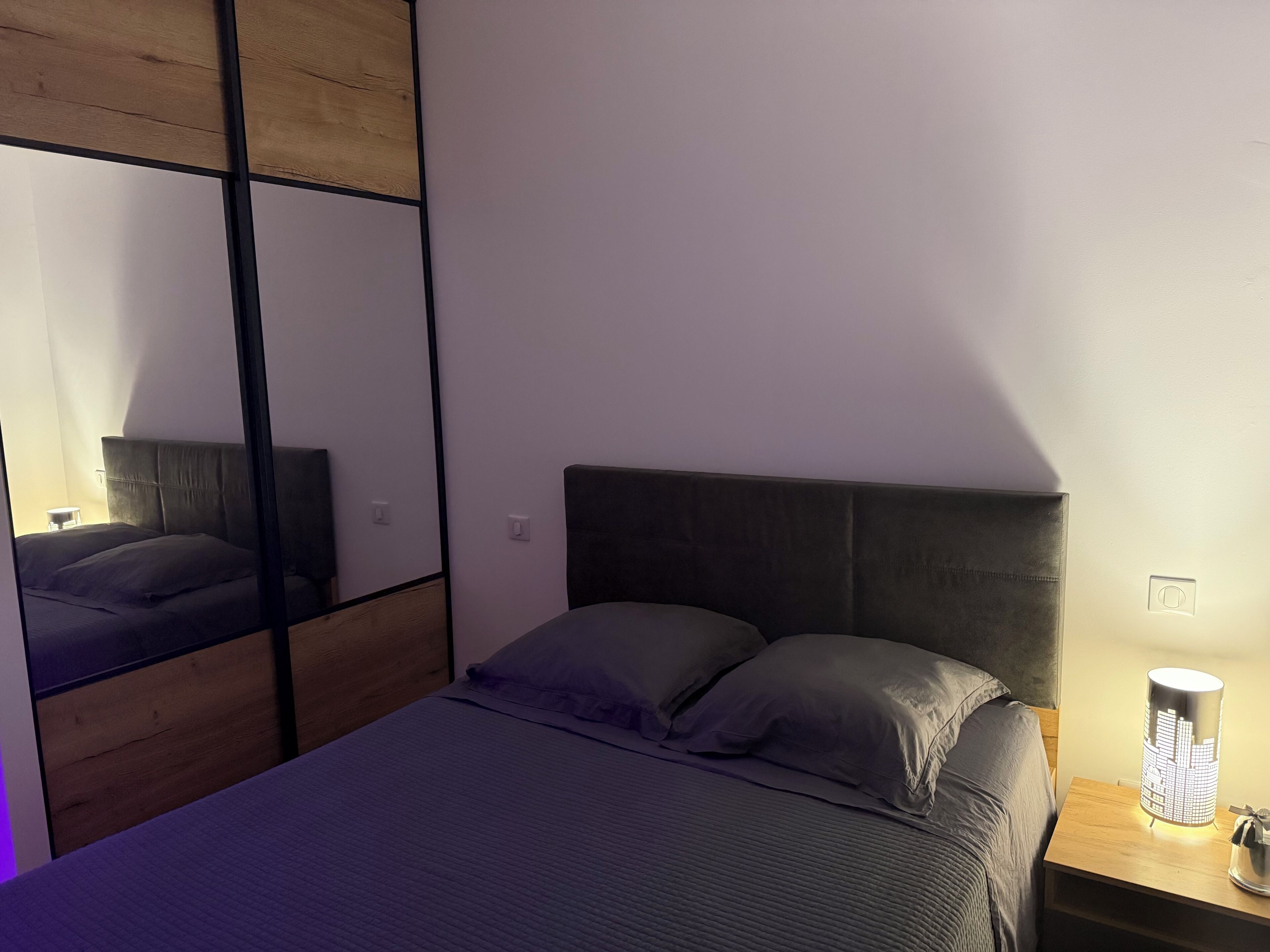 Una camera da letto con un letto, un comodino, una lampada e uno specchio.