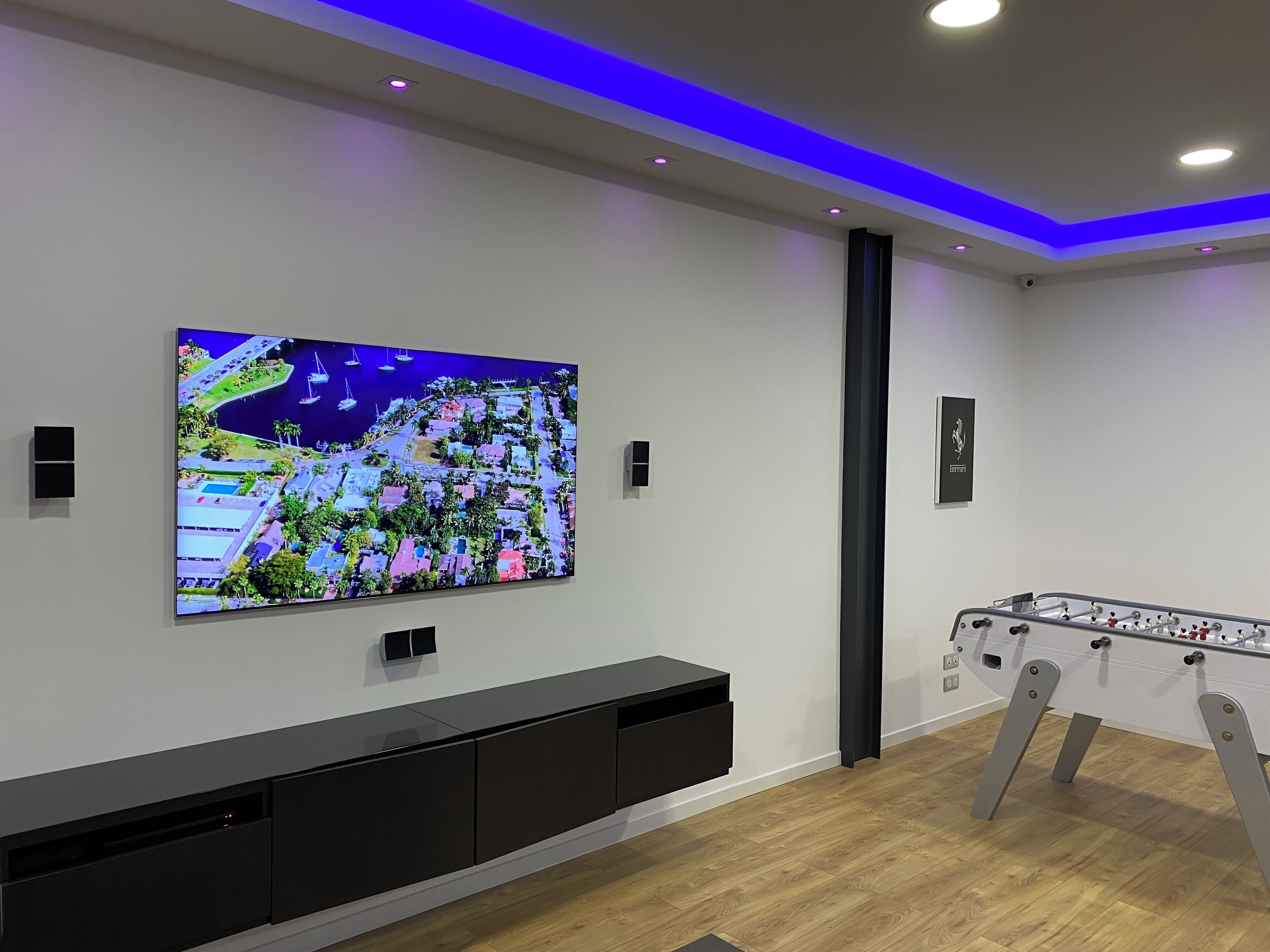 Una sala de estar moderna con un televisor de pantalla plana grande montado en la pared, un mueble negro de entretenimiento debajo y una mesa de fútbol de mesa a la derecha.