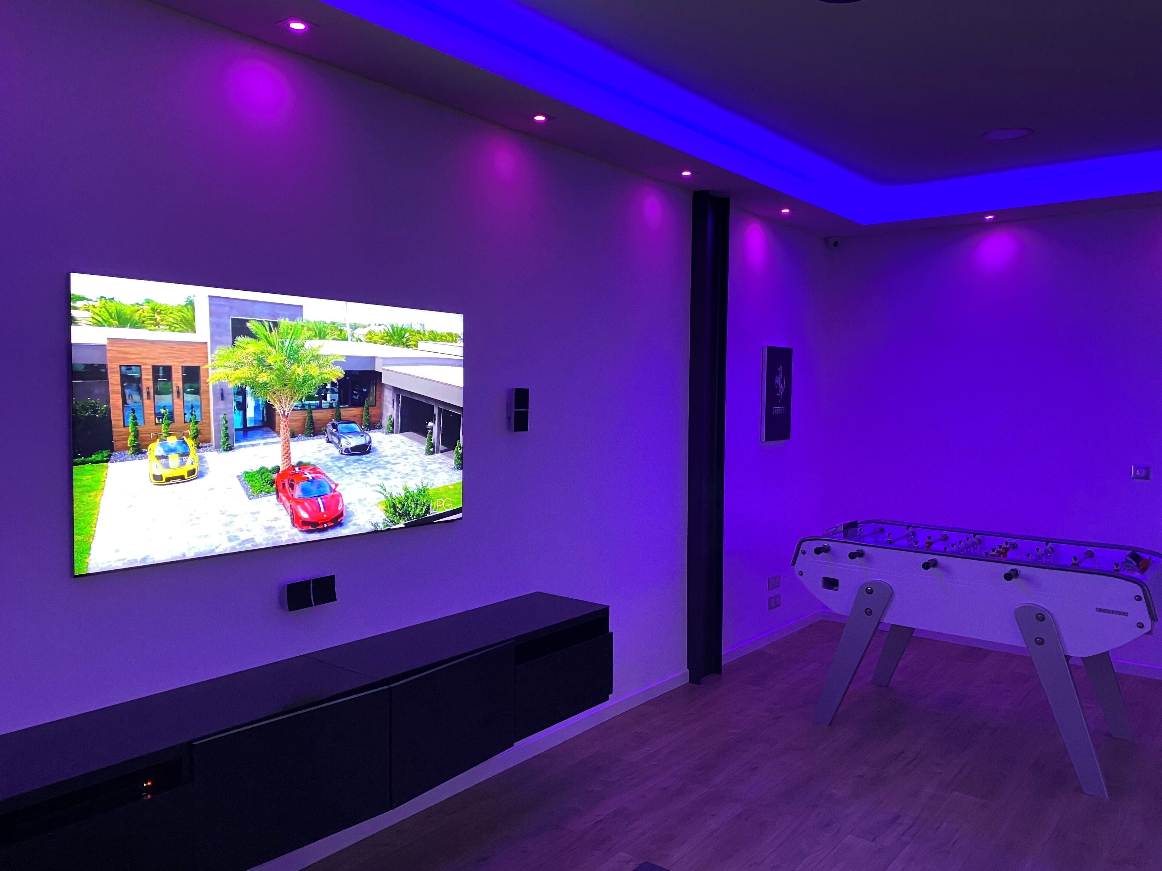 Habitació moderna amb televisió de pantalla plana penjada a la paret, taula de futbolí i moble d'entreteniment fosc.