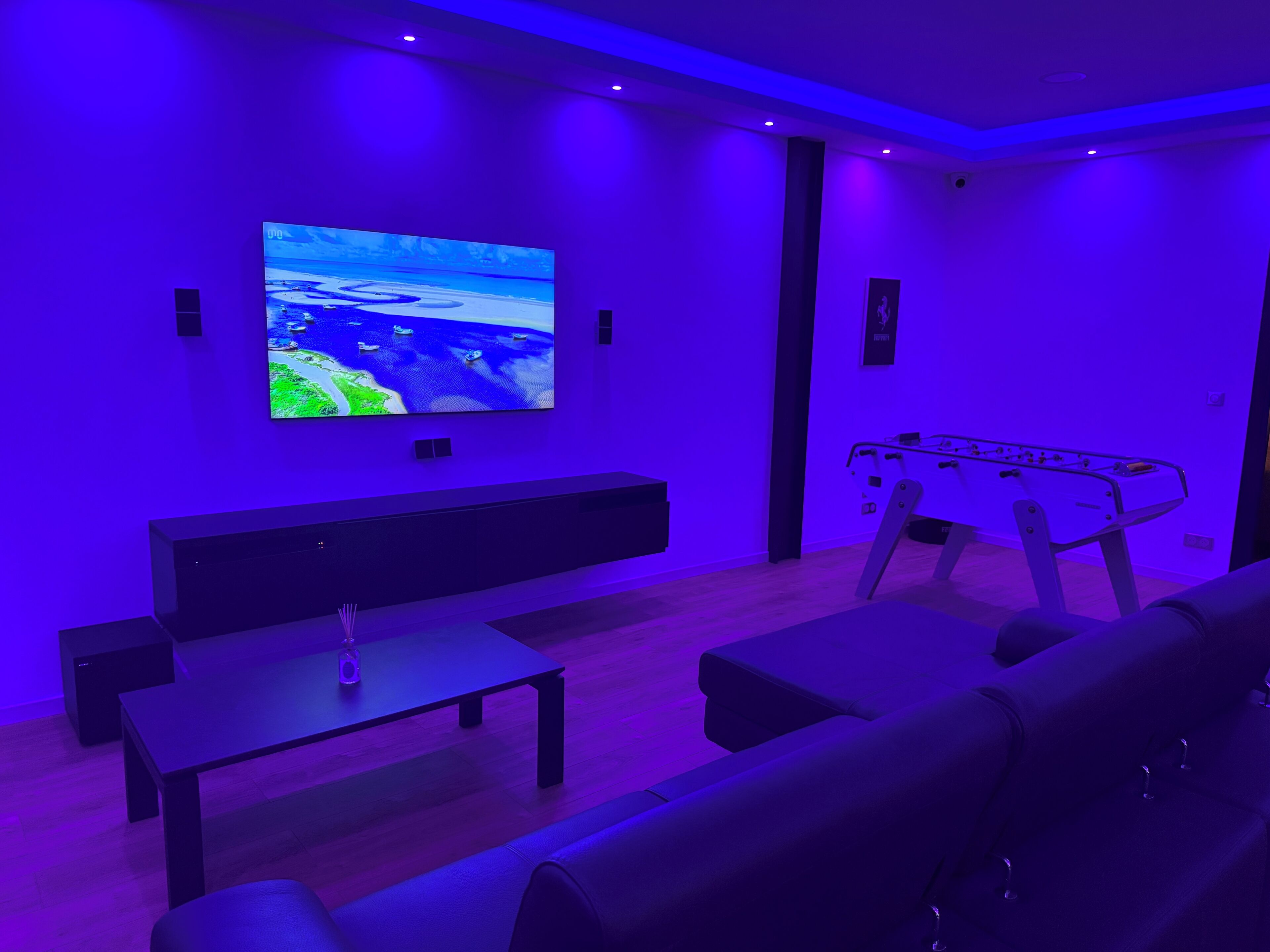 A modern living room with a flat-screen TV mounted on the wall, a foosball table, a sofa, and a coffee table.