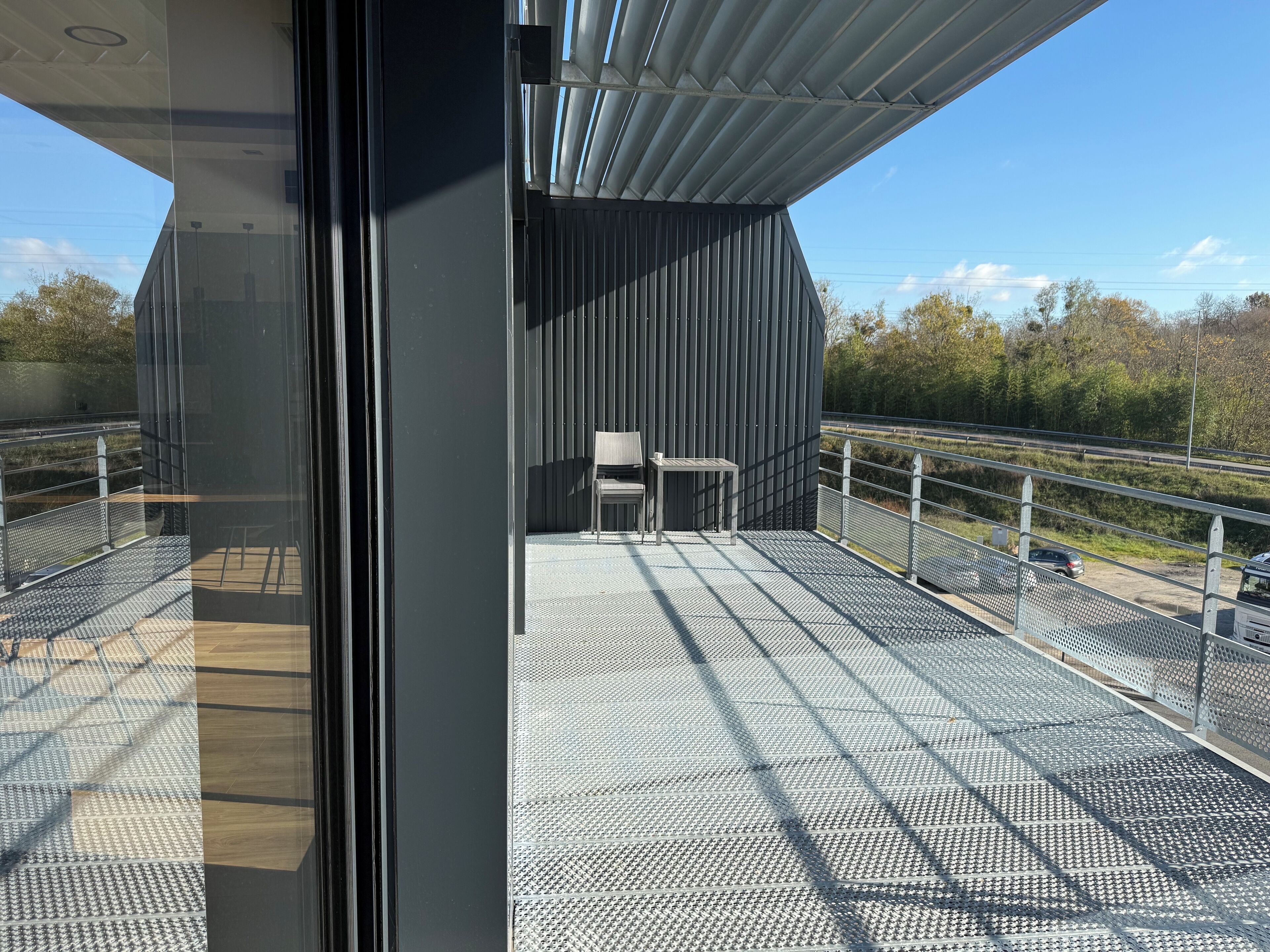 A modern balcony with a metal railing, a chair, and a table.
