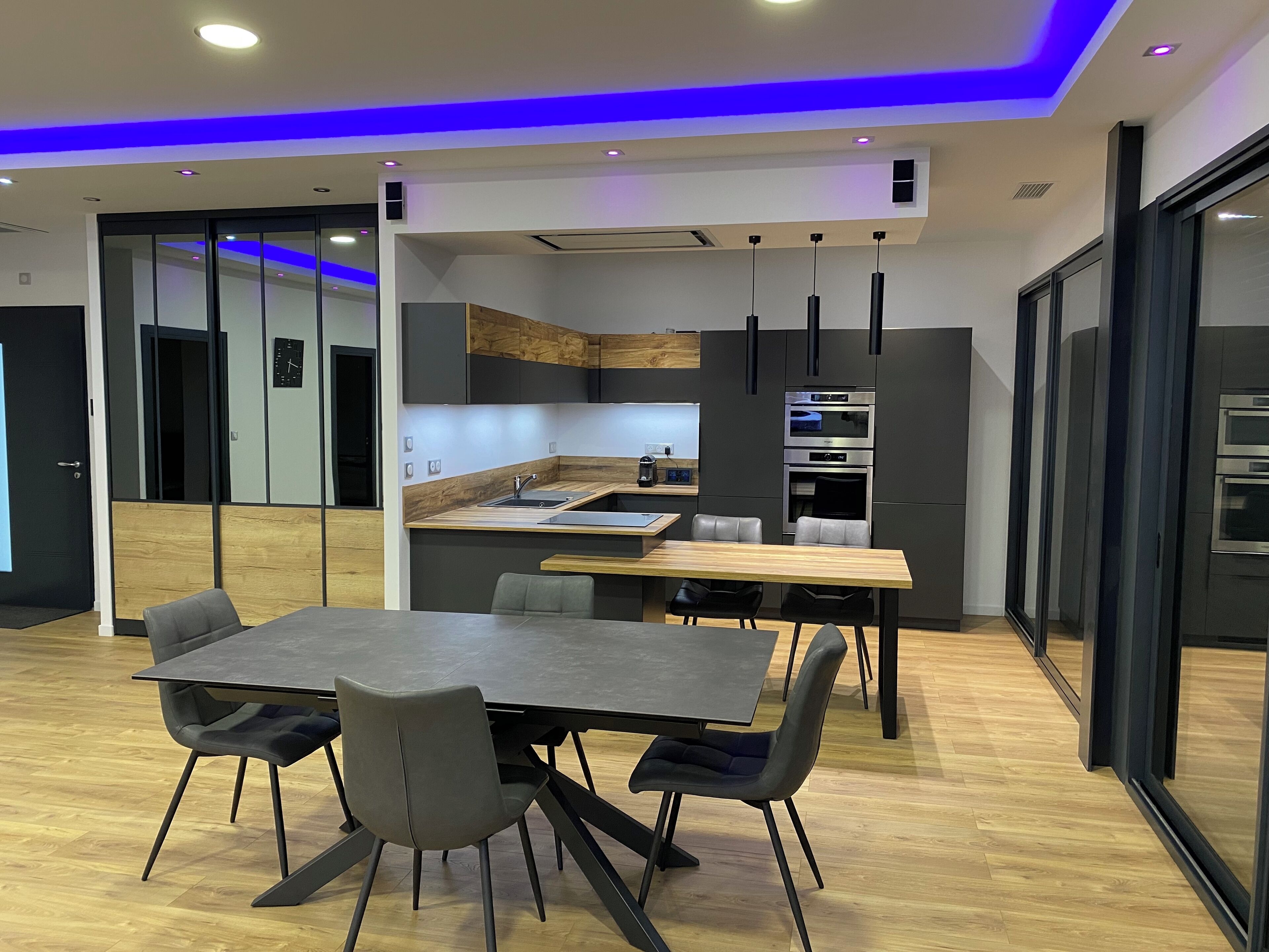 A modern kitchen with a central island, built-in appliances, and a dining area with a table and chairs.