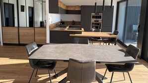A modern kitchen with a central island, a dining area with a large table and chairs, and a view of the outdoors through a sliding door. - Magnificent luxury loft with top-of-the-range amenities. (Montussan)