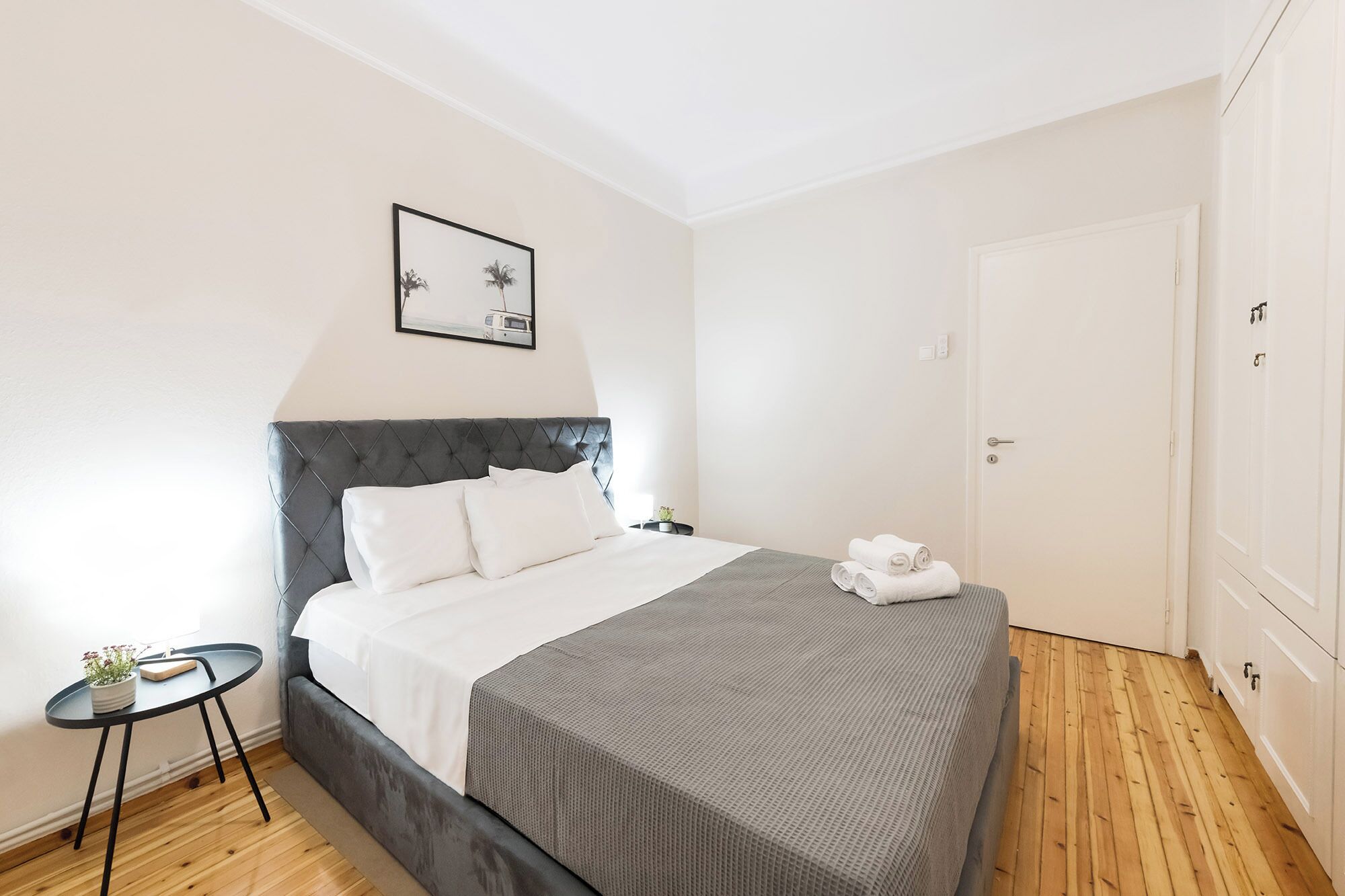 Une chambre à coucher bien rangée, avec un lit, une petite table de chevet, un tableau encadré au mur et une armoire.