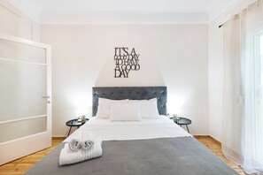 A neatly arranged bedroom with a tufted headboard, a bed with white linens, a grey throw blanket, and a motivational quote on the wall. - Portoseaview Apartments A Svolou 53 (Thessaloniki)