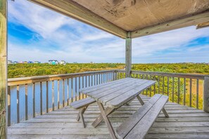 Eine Holzterrasse mit Picknicktisch und Geländer, mit Blick auf eine Küstenlandschaft mit Häusern und Vegetation.
