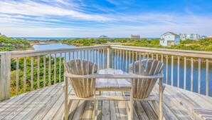 Een houten terras met twee Adirondack-stoelen, gericht op een waterpartij en een verre kustlijn met huizen.