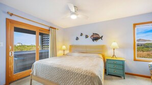 Een slaapkamer met een bed, een plafondventilator, een raam met uitzicht, een nachtkastje en een deur naar een balkon.