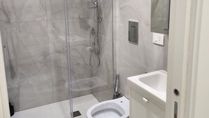 Ett modernt badrum med en dusch som är avskärmad med glasväggar, en toalett och ett handfat.