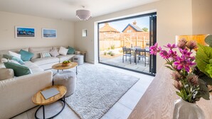 A modern living room with a sofa, coffee table, and a view of the backyard through a glass door. - Nethercoat, Wells-next-the-Sea, Norfolk (Wells-next-the-Sea)