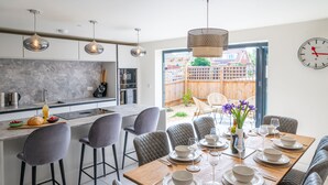 A modern kitchen with a marble backsplash, a dining area with a wooden table set for six, and a view of a backyard through a glass door. - Nethercoat, Wells-next-the-Sea, Norfolk (Wells-next-the-Sea)