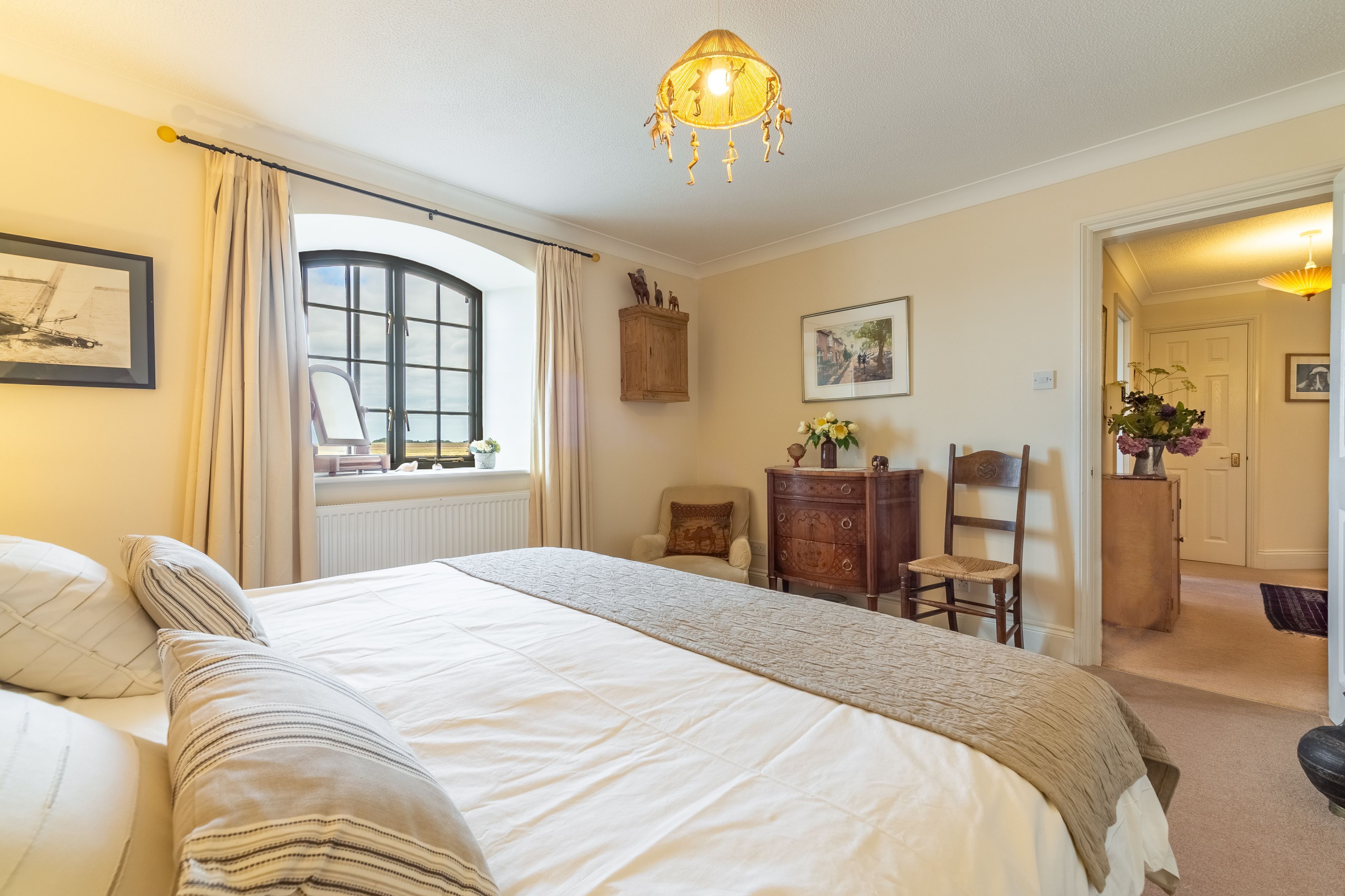 A well-lit bedroom with a large bed, a window with curtains, a wooden dresser, and a chair.