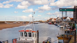 Un porto con imbarcazioni ormeggiate, un edificio con la scritta "PORT OF WELLS" e cielo sereno con nuvole.