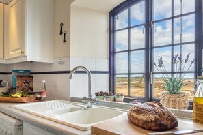 Eine Küche mit einem großen Fenster, einer Spüle, einem Brotlaib und einer Flasche Olivenöl auf der Arbeitsfläche.