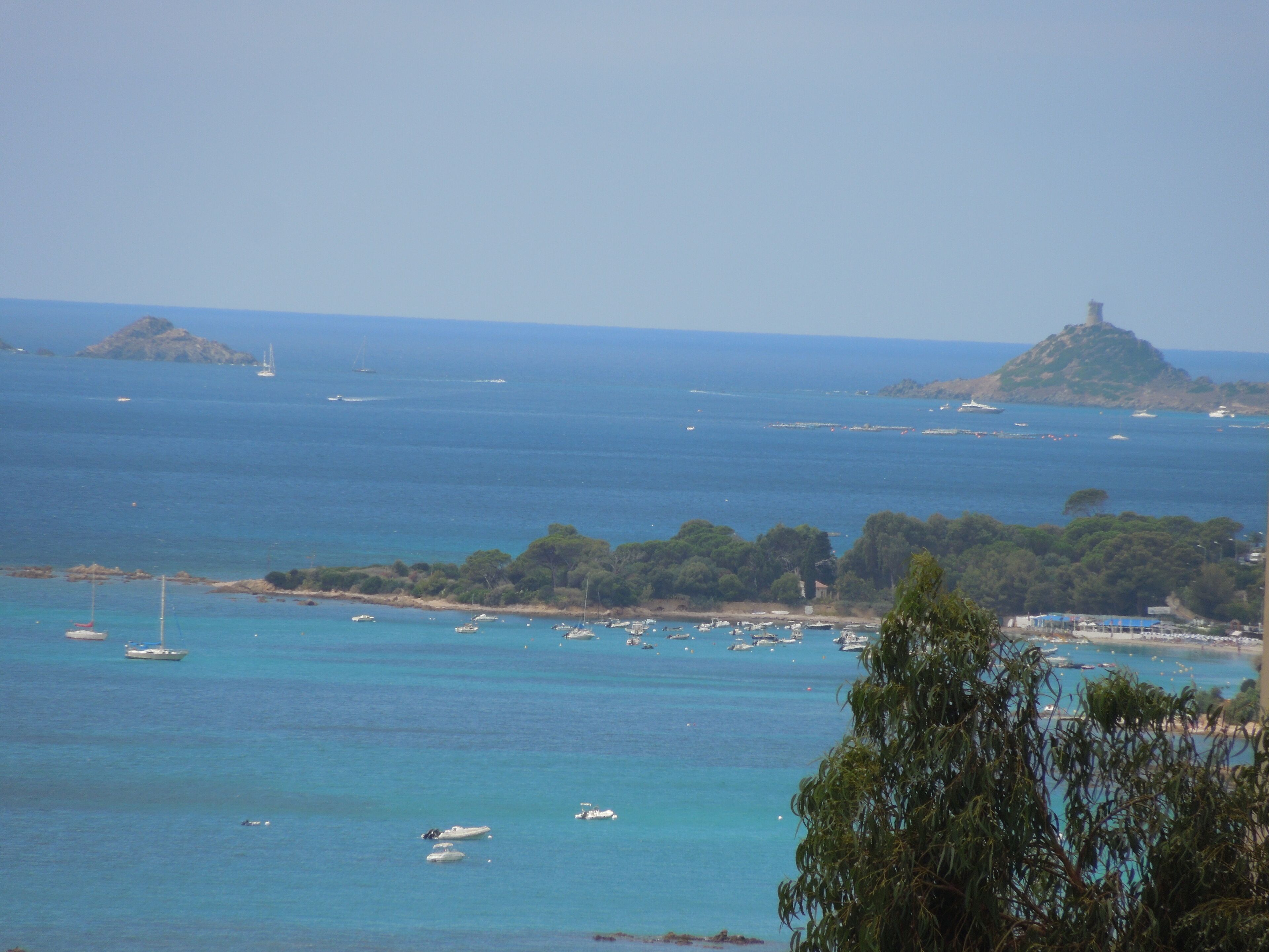 Une vue sur la côte, avec des bateaux, un phare et une île boisée.