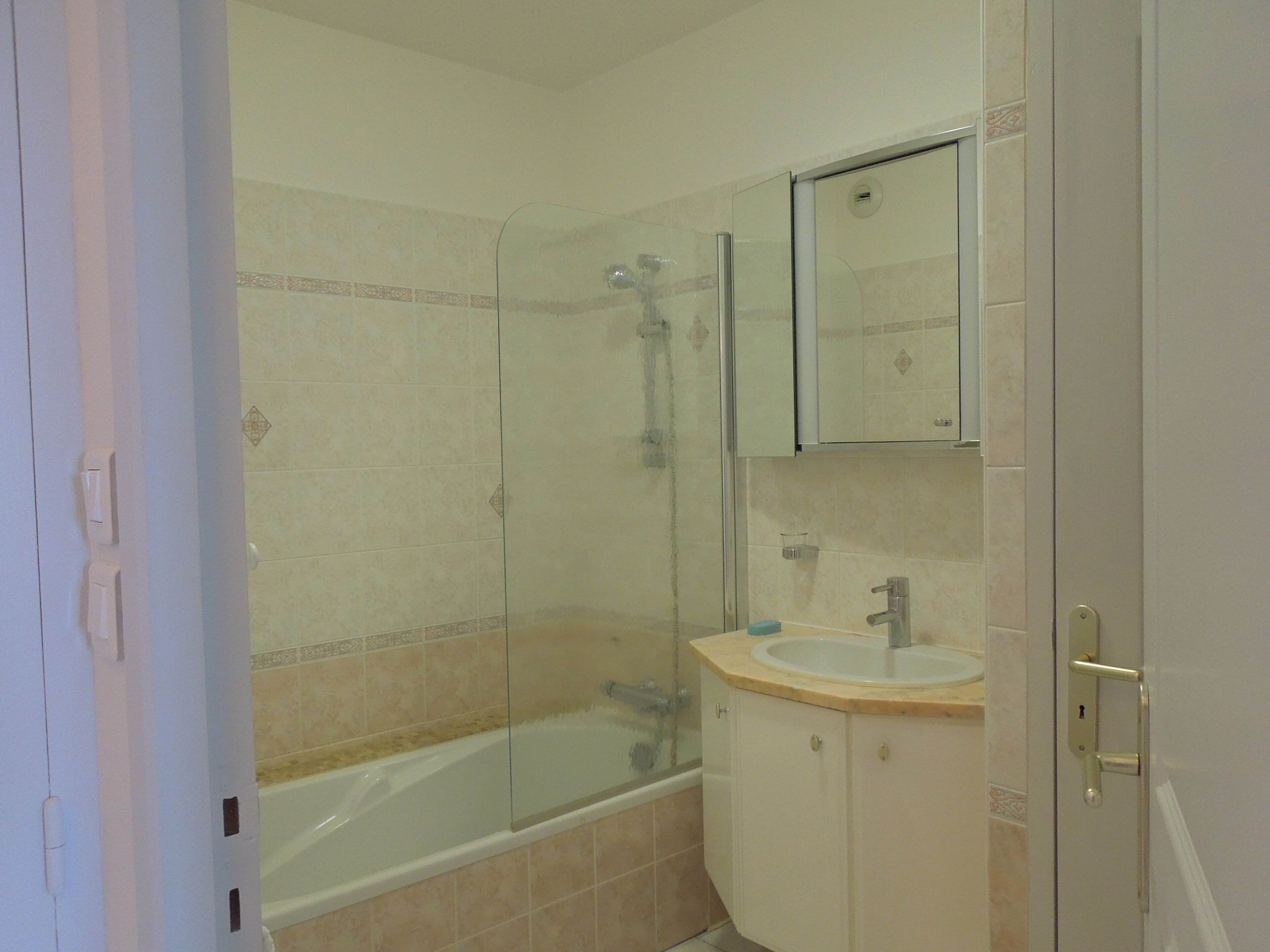 A bathroom with a glass-enclosed shower, a bathtub, a sink with a mirror above it, and a door with a handle.
