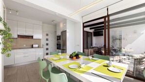 A modern kitchen with white cabinets, a dining area with green chairs, and a large window overlooking a balcony. - Sea Breeze Jarea by Escape Home (Playa Blanca)