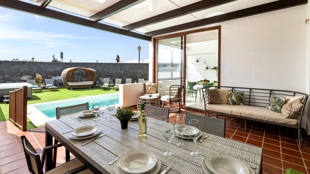A dining area with a table set for four, a sofa, and a pool in the background. - Sea Breeze Jarea by Escape Home (Playa Blanca)