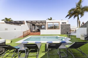 Een modern buitenzwembadgedeelte met ligbedden, een jacuzzi en een terras met een stenen muur en een palmboom.