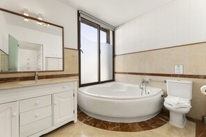 Een moderne badkamer met een ruime badkuip, toilet en een wastafel met lades.