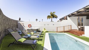 Ein Poolbereich mit Liegestühlen, einem kleinen Tisch und einer Terrasse mit Geländer.