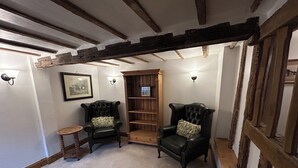 Una habitación con vigas de madera a la vista, dos sillones de cuero con cojines estampados, una mesita redonda y una estantería.