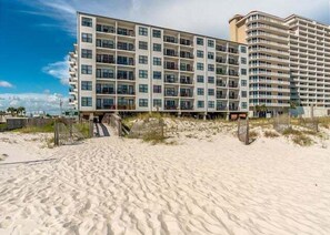 Ein Strandhotel mit mehreren Etagen, Balkonen und einem Sandstrand davor.