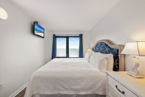 Ein Schlafzimmer mit einem Bett, einem Nachttisch, einer Lampe, einem Fernseher und einem Fenster mit Vorhängen.