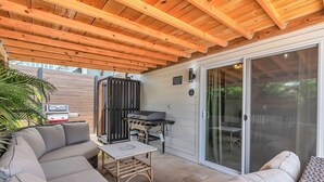Une terrasse extérieure couverte, équipée d’un barbecue, d’un espace salon et de portes-fenêtres coulissantes.