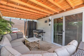 Eine überdachte Terrasse im Freien mit Grill, Sitzgelegenheit und Glastüren.
