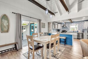 A modern kitchen with a blue island, wooden chairs, and a dining table with placemats. - 🌞🌴Single Family Home | Walk to Beach | Rocking Sunset Beach House (Treasure Island)